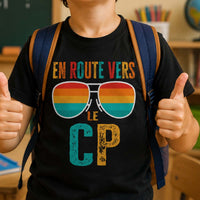 Garçon souriant en classe de CP avec son sac à dos, heureux de faire sa rentrée scolaire, portant un T-shirt humoristique « En route vers le CP ».