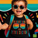 Enfant de 2 à 3 ans portant un t-shirt noir "En route vers la Petite Section", souriant avec un sac à dos et des lunettes colorées, prêt pour sa première rentrée à l'école maternelle