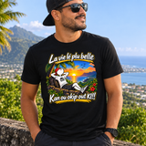 Homme portant un t-shirt noir avec illustration d’un coucher de soleil tropical et texte créole, devant un paysage côtier de La Réunion.
