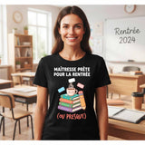 T-shirt noir de femme porté dans une salle de classe, avec le design "MAÎTRESSE PRÊTE POUR LA RENTRÉE (OU PRESQUE)" et l'illustration de livres, d'une tasse de café et d'un crayon kawaii