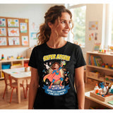 T-shirt noir de femme porté dans une classe d'école, avec le design 'Super ATSEM' illustré d'une super-héroïne tenant une compote et entourée d'objets de classe et du texte 'Ouvre les compotes d'une seule main'