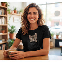 T-shirt noir de femme en coton, avec l'illustration en trompe-l'œil d'un chaton tigré sortant de la poche de poitrine, porté par une femme souriante dans un environnement de café lumineux.