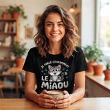T-shirt noir pour femme en coton, porté par une jeune femme souriante dans un café lumineux, avec l'illustration d'un chaton gris et le texte blanc "JE PARLE COURAMMENT LE MIAOU" et des empreintes de pattes