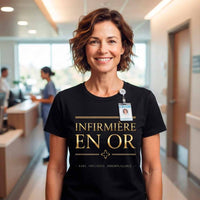 T-shirt noir pour femme en coton, porté par une infirmière souriante dans une unité de soins moderne. Le design "INFIRMIÈRE EN OR" avec le texte doré et la croix est clairement visible et centré
