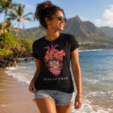 Femme portant un t-shirt noir avec le design « 974 Dans le Cœur » marchant les pieds dans l'eau sur une plage de l'île de La Réunion avec les montagnes en arrière-plan.