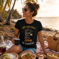 Femme portant un t-shirt noir avec le design « Chef Cari Poulet du Dimanche » lors d'un pique-nique au bord de la plage avec un repas créole à La Réunion