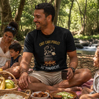 Homme portant un t-shirt noir avec le design « Chef Cari Poulet du Dimanche » lors d'un pique-nique en famille dans une forêt à La Réunion.