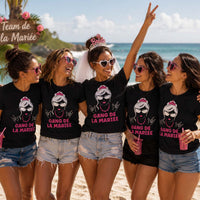 Groupe de femmes portant un t-shirt noir avec le design « Gang de la Mariée » lors d'un enterrement de vie de jeune fille sur une plage tropicale à La Réunion, avec la future mariée au centre portant un voile et un diadème.