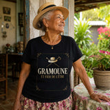 Femme âgée portant un t-shirt noir avec le design « Gramoune et fier de l'être » sur la varangue d'une maison créole entourée d'un jardin tropical à La Réunion.