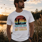 Homme portant un t-shirt blanc avec le design « Hunting Dad Like a Regular Dad But Cooler », debout près d'un marais au coucher du soleil, dans un décor naturel avec roseaux, oiseaux en vol et ambiance de chasse.