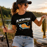 Femme portant un t-shirt noir avec l'inscription « Je m'en Fish Complètement », tenant une canne à pêche et montrant fièrement un poisson fraîchement pêché au bord d'un lac au coucher du soleil, dans une ambiance naturelle et paisible.