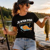 Femme portant un t-shirt noir avec l'inscription « Je m'en Fish Complètement », tenant une canne à pêche et montrant fièrement un poisson fraîchement pêché au bord d'un lac au coucher du soleil, dans une ambiance naturelle et paisible.
