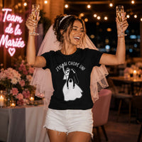 Future mariée portant un t-shirt noir avec le design « J'en ai chopé un ! », levant deux coupes de champagne avec un grand sourire lors de sa soirée d'enterrement de vie de jeune fille