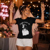 Future mariée portant un t-shirt noir avec le design « J'en ai chopé un ! », levant deux coupes de champagne avec un grand sourire lors de sa soirée d'enterrement de vie de jeune fille