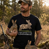 Homme portant un t-shirt noir avec une illustration de lapin sauvage et le texte « Le lapin sauvage m'invite, la forêt m'attend ! », photographié dans une clairière en forêt entouré de plusieurs lapins sauvages au coucher du soleil.