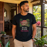 Homme portant un t-shirt noir avec le design « Ma Case, Ma Kour, Mon Paradis » sur la varangue d'une maison créole traditionnelle entourée d'un jardin tropical à l'île de La Réunion.