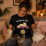 Femme portant un t-shirt noir avec le design « Maman de Chat » assise dans un salon chaleureux en caressant plusieurs chats confortablement installés autour d'elle.