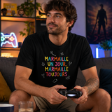 Homme portant un t-shirt noir avec le design « Marmaille un jour, marmaille toujours » assis sur un canapé en train de jouer à la console dans un salon.