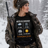 Femme portant un t-shirt noir avec l'inscription « Météo du Chasseur », avançant dans une forêt enneigée sous une chute de neige, vêtue d'une tenue de chasse hivernale, dans une ambiance froide et montagneuse.