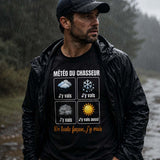 Homme portant un t-shirt noir avec l'inscription « Météo du Chasseur », marchant sous une pluie battante sur un chemin forestier, équipé d'une veste imperméable, dans une ambiance de chasse automnale.