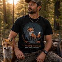 Homme portant un t-shirt noir avec une illustration de renard et le texte « Le renard m'attend, il est temps de partir ! », photographié en forêt aux côtés d'un renard dans un décor boisé au coucher du soleil.