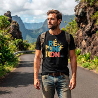 Un homme barbu portant le t-shirt noir se tient sur une route de montagne asphaltée à La Réunion. Il a un sac à dos et porte un jean. Le design 