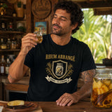 Homme portant un t-shirt noir avec le design « Rhum Arrangé » en train de déguster un petit verre de rhum arrangé dans un bar créole à La Réunion