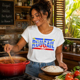 Jeune femme portant un t-shirt blanc avec le design « Rougail 974 » en cuisinant un rougail saucisse avec un plat de riz dans une cuisine réunionnaise chaleureuse.