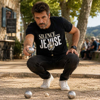 Homme portant un t-shirt noir avec le design « Silence... Je Vise » en pleine partie de pétanque sur un boulodrome en visant le cochonnet avec concentration.