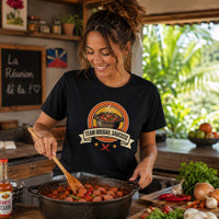 Femme portant un t-shirt noir avec le design « Team Rougail Saucisse » en train de préparer un rougail saucisse dans une cuisine créole à La Réunion