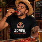Homme portant un t-shirt noir avec le design « Zoreil mais presque créole » en train de manger un piment rouge dans un restaurant créole.